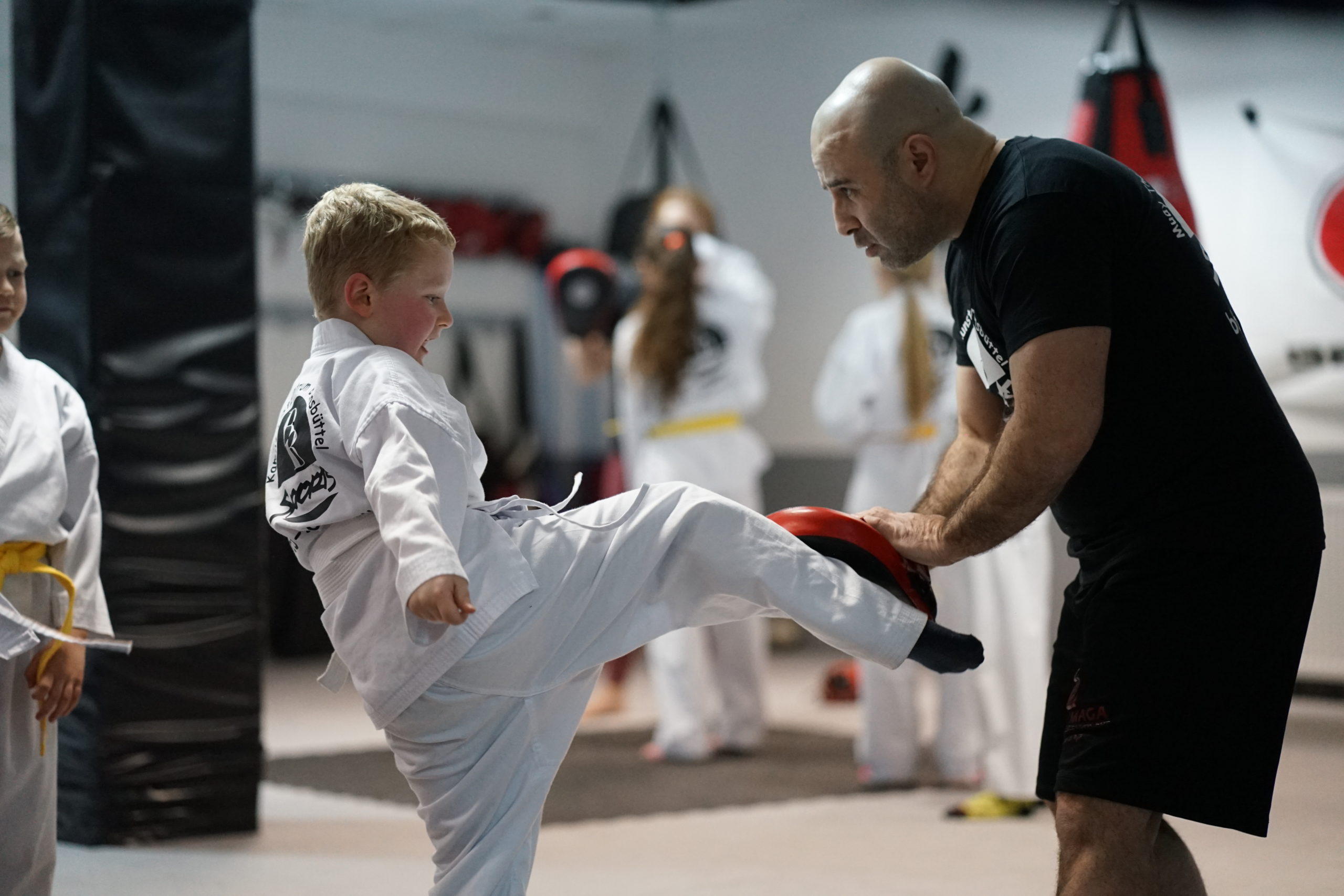 Kickboxen Kids: Kind tritt gegen ein Polster, das der Trainer hält.